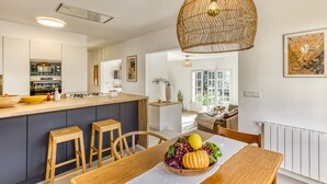 A modern kitchen with a central island, wooden stools, and a dining table with a fruit bowl. - Villa 'Les Aulines' with Mountain View, Wi-Fi and Air Conditioning (Calonge)