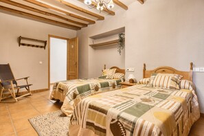 Een slaapkamer met twee bedden, houten balken in het plafond, een stoel en een klein tafeltje.