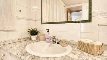 Un baño con un lavabo blanco, un espejo de marco verde, una planta en maceta, un dispensador de jabón y una cesta de papel higiénico.