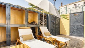 A sunlit outdoor lounge area with wooden loungers and a covered seating area, adjacent to a building with a metal gate and a sign reading 'SALIDA'. - Country House 'Casa Amparo' with Mountain View, Private Pool and Wi-Fi (Alcoleja)