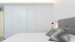 Un dormitorio con cama, almohadas, cabecera, armario y mesita de noche.