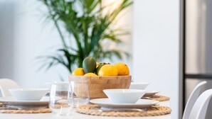 Una mesa de comedor dispuesta con platos blancos, tazones y un cuenco de madera con frutas.