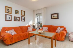 Una sala de estar con dos sofás naranjas, una mesa de centro de vidrio y varias fotografías enmarcadas en la pared.