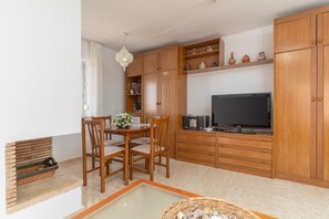 Una cocina moderna con armarios de madera, una mesa de comedor con sillas, un televisor y un estante decorativo.