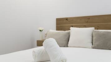 Een opgemaakt bed met witte lakens, een houten hoofdbord en een vaas met witte bloemen op een nachtkastje.