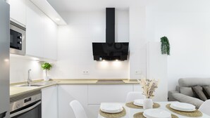A modern kitchen with white cabinets, a black range hood, and a dining area with a glass table and white chairs. - Apartment 'Calderon' with Air Conditioning (Barbate)