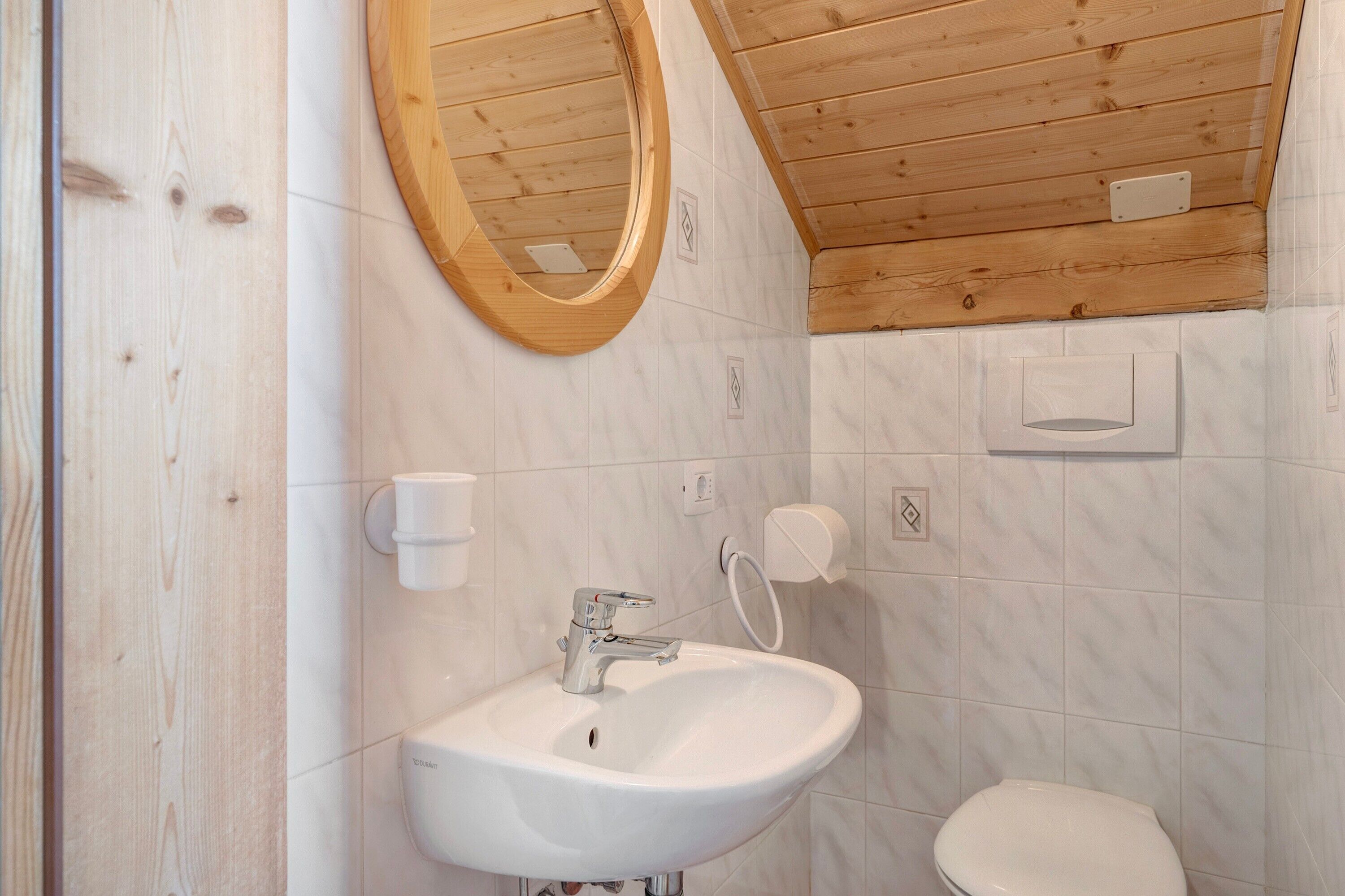 A bathroom with a wooden ceiling, a white sink, a toilet, and a mirror.
