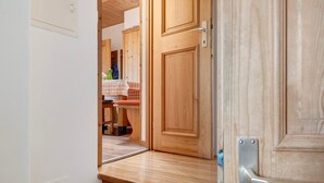 Une porte en bois avec une poignée en métal, un plancher en bois et, au fond, une table recouverte d’une nappe à carreaux.