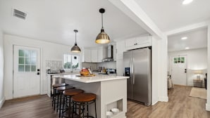 Et moderne køkken med en central ø, rustfrit stål-hvidevarer og hængende lamper.