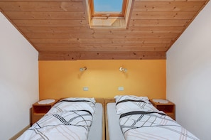 Une chambre avec deux lits, un plafond en bois et une lucarne.