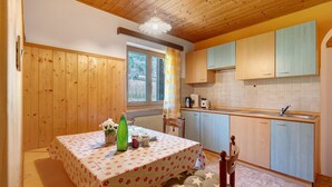 A kitchen with wooden cabinets, a dining table with a floral tablecloth, and a window with curtains. - Apartment 'Theresa' with Mountain View, Shared Garden and Wi-Fi (Appiano)