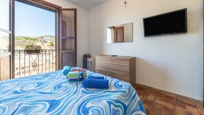 Ein Schlafzimmer mit Bett, Fernseher, einem Holzschrank und einem Balkon mit Blick auf Gebäude.
