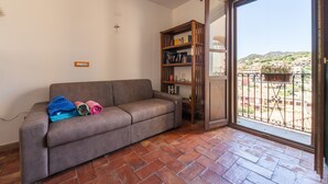 Ein Wohnzimmer mit einer Couch, einem Bücherregal und einer Schiebetür zum Balkon.