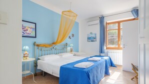 Een slaapkamer met twee bedden, een raam met gordijnen, een nachtkastje met een lamp en een muur met een ingelijste foto.