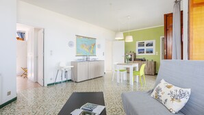 Een woonkamer met een bank, een salontafel met tijdschriften, een kaart aan de muur, en een eethoek met een tafel en stoelen.