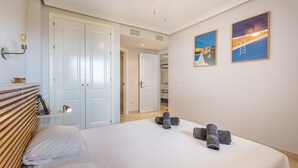 Ein Hotelzimmer mit einem Bett, einer Nachttischlampe, einem Handtuchhalter und zwei gerahmten Bildern an der Wand.