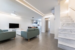 Ein modernes Wohnzimmer mit Fernseher, zwei Sofas, einem Couchtisch und einer Küche im Hintergrund.
