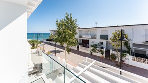 Un balcón con vistas despejadas al mar, un edificio blanco con balcones y un árbol.