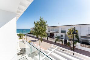 Un balcón con vistas despejadas al mar, un edificio blanco con balcones y un árbol.