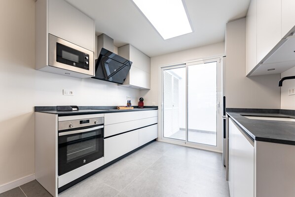 Una cocina moderna con electrodomésticos integrados, un amplio ventanal y una puerta corrediza de vidrio.