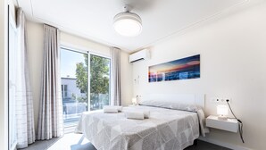 Un dormitorio moderno con una cama grande, una mesita de noche con lámpara, aire acondicionado de pared y un ventanal con cortinas.