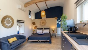Habitación compacta con cama, sofá, zona de cocina y un amplio ventanal.