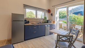 Una cocina moderna con refrigerador, estufa y lavavajillas, una mesa de comedor con sillas y un ventanal corredizo que da a un patio exterior.