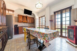 A kitchen with patterned tiles, wooden cabinets, a dining table with a colorful tablecloth, and a television mounted on the wall.