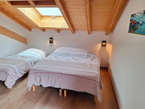 Una habitación con dos camas, vigas de madera, un tragaluz y luces fijadas en la pared.