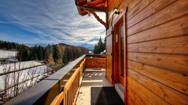 Een houten chalet met balkon, met uitzicht op een besneeerd landschap en bergen.