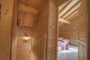 Un intérieur en bois avec un escalier, un lit recouvert d’une couverture à motifs et un luminaire fixé au mur.