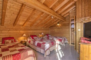 A cabin with two beds, wooden walls, a ceiling with wooden beams, and a television on a wooden cabinet.