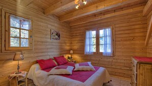 Een houten kamer met een bed, een nachtkastje, een lamp en een raam met gordijnen.
