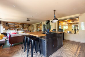 A spacious kitchen with a central island, bar stools, and a large bookshelf filled with books. - Villa "Osez Adélaïde" with Private Indoor Pool (La Ciotat)