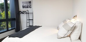 A bedroom with a bunk bed, a black metal ladder, a white bed with pillows, a black throw blanket, a wall-mounted light, and a window with a view of greenery. - Villa "Osez Adélaïde" with Private Indoor Pool (La Ciotat)