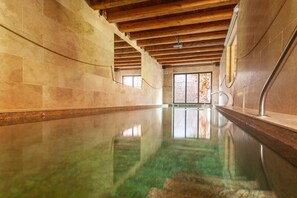 Ein großes Hallenbad mit Holzbalkendecke und Steinwänden.