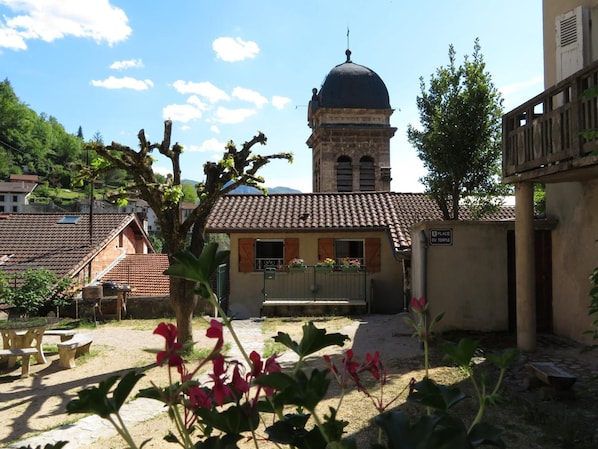Un patio con un edificio que presenta una cúpula, un banco de piedra y un cartel que indica un lugar de culto.