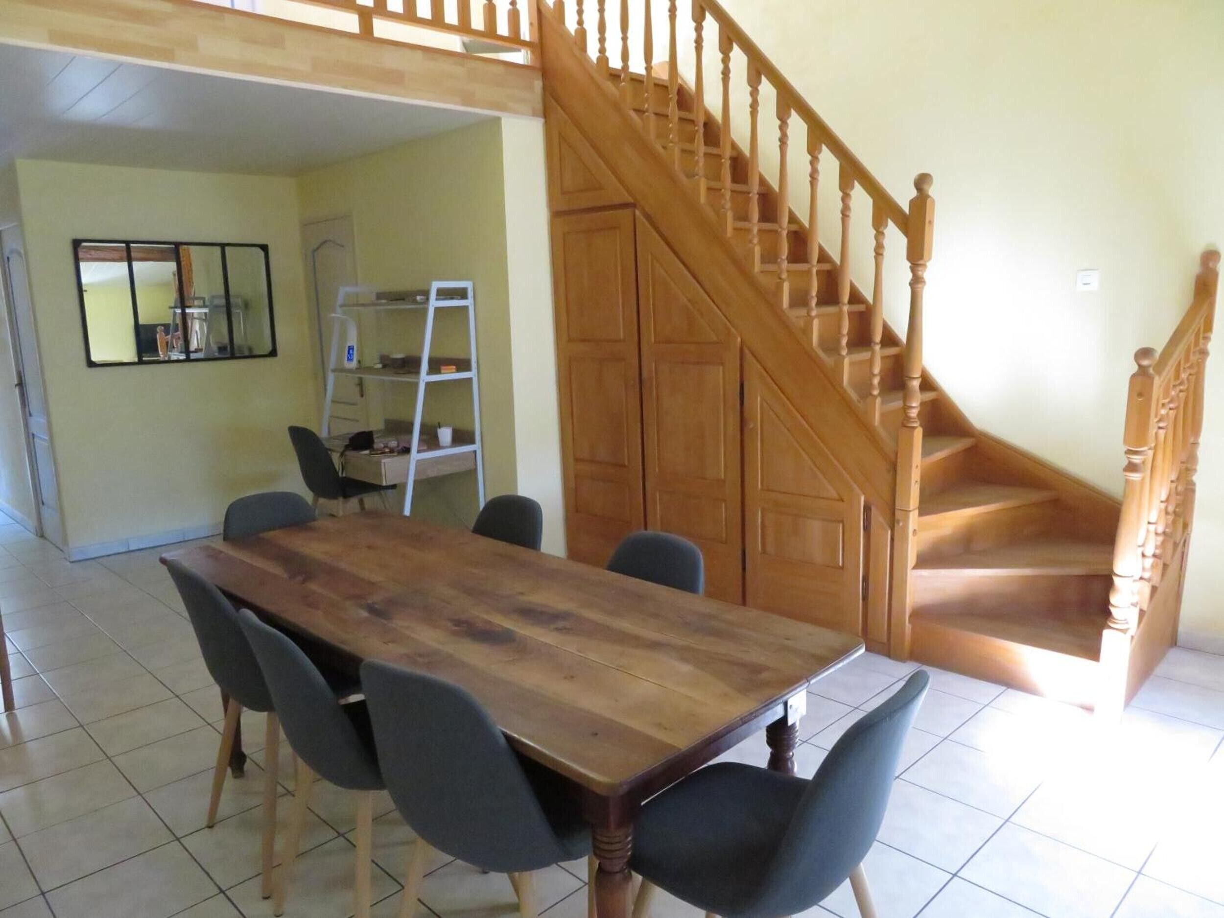 A dining area with a wooden table and chairs, a staircase, and a mirrored wall.