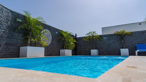 A swimming pool with a stone wall, palm trees, and lounge chairs. - Apartment 'Apartamento Dialma' with Mountain Views, Wi-Fi, and Air Conditioning (Vejer de la Frontera)