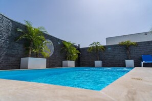Una piscina con pared de piedra, palmeras y sillas de descanso.