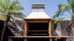 A brick-built outdoor kitchen with a chimney, surrounded by stone walls and palm trees. - Apartment 'Apartamento Dialma' with Mountain Views, Wi-Fi, and Air Conditioning (Vejer de la Frontera)