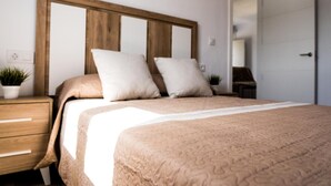 A bedroom with a wooden headboard, two white pillows, a beige bedspread, a nightstand with a plant, and a door leading to another room. - Apartment 'Apartamento Dialma' with Mountain Views, Wi-Fi, and Air Conditioning (Vejer de la Frontera)