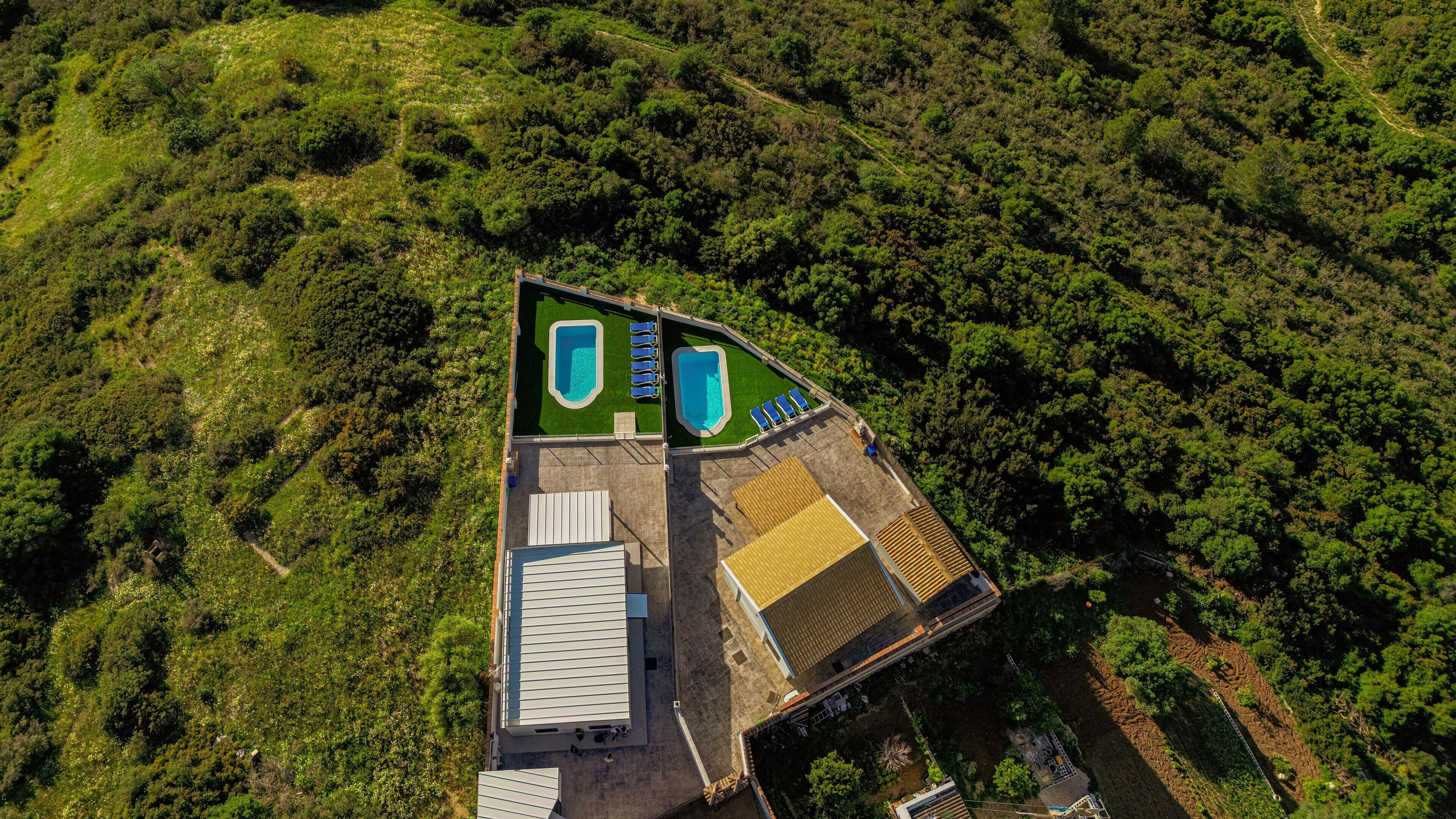Vue aérienne d’un complexe hôtelier doté de deux piscines, d’un espace couvert et d’un bâtiment avec un toit en pente.