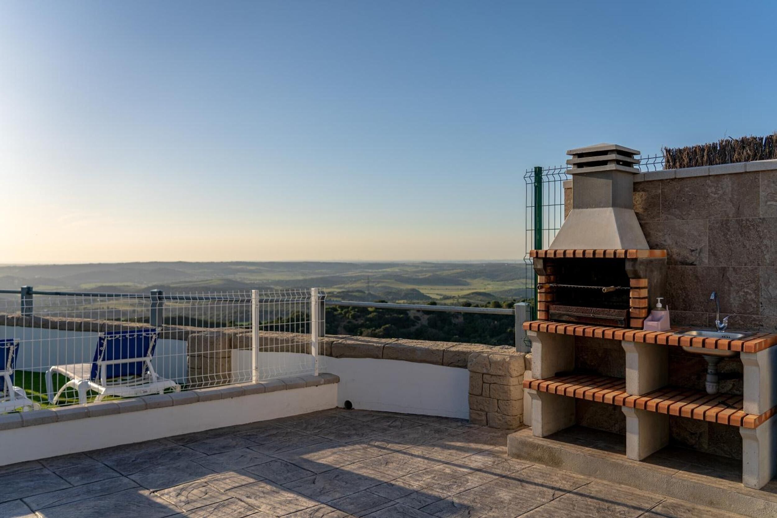 A rooftop patio with a barbecue grill, a pool, and a view of the countryside.
