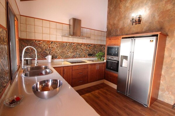 Una cocina con un lavamanos doble, electrodomésticos de acero inoxidable, armarios de madera y salpicadero de azulejos.