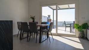 Un coin repas avec une table et des chaises, une plante en pot, et une vue sur un espace extérieur aménagé en salon, visible à travers une porte vitrée.