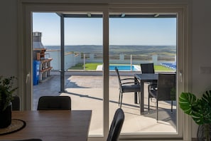 An open sliding glass door leading to an outdoor patio with a pool, chairs, and a grill.