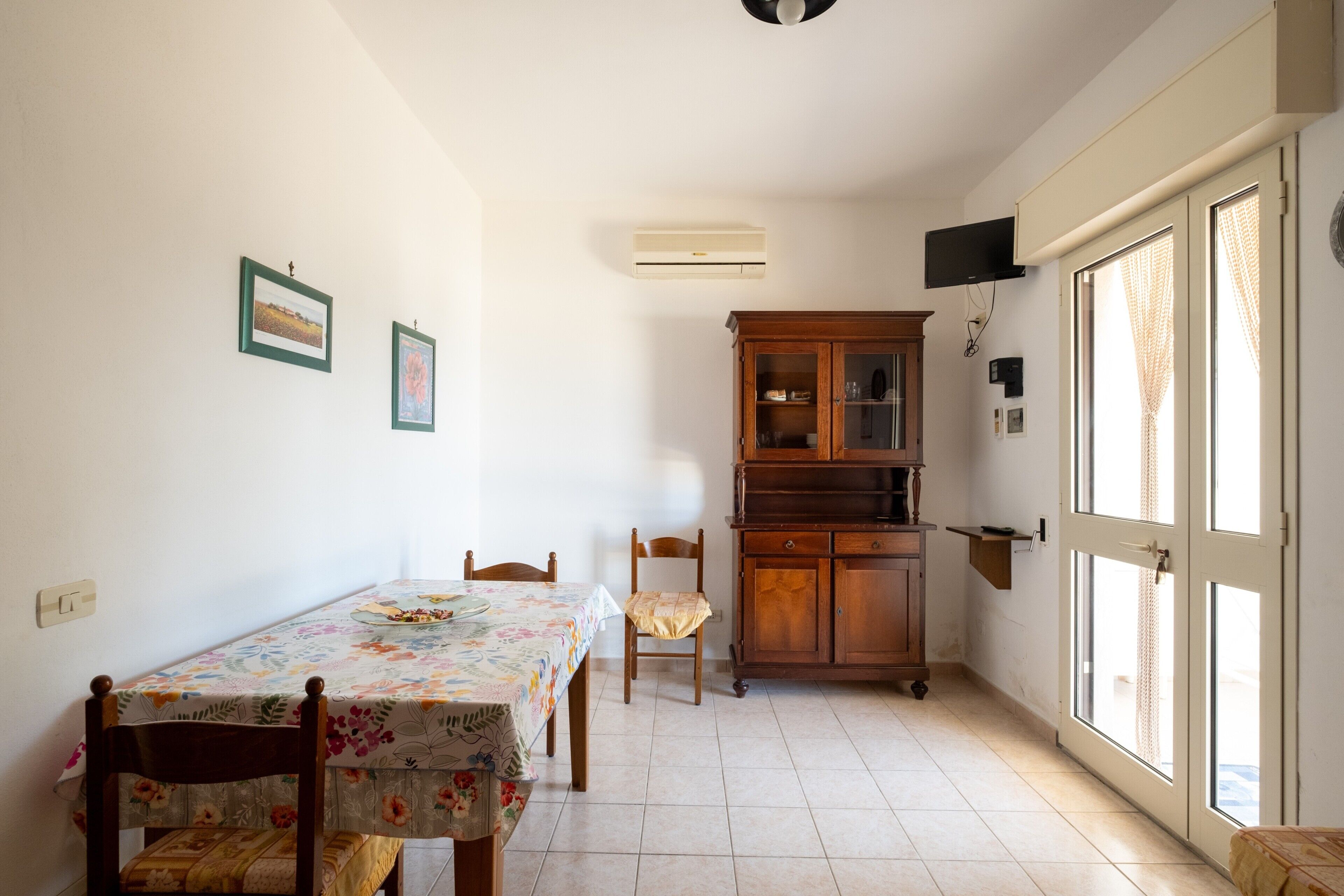 Un coin repas comprenant une table, des chaises, un buffet et une porte avec des rideaux.
