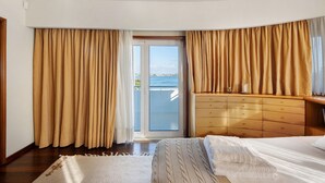 Una camera da letto con un letto, una cassettiera in legno, una finestra con tende e vista sul mare.