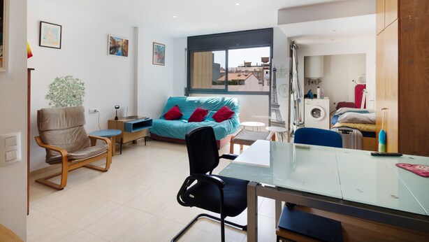 Una sala de estar moderna con un sofá, una silla, una mesa de comedor y un ventanal con vistas a edificios.